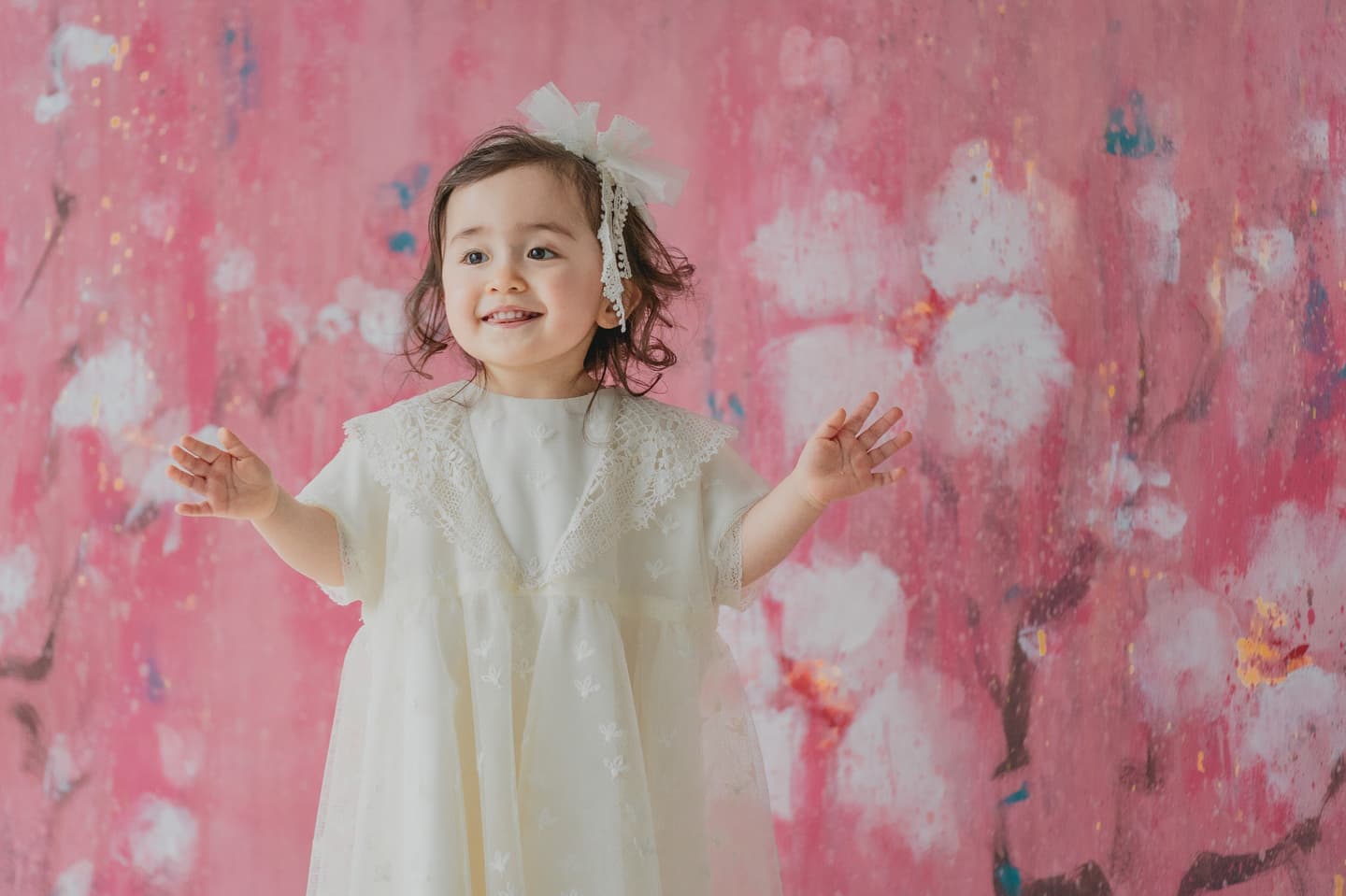 花柄の壁紙の前で白いドレスを着た女の子の写真